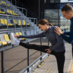 Athlete doing stretching with coach during sports performance training session outdoors