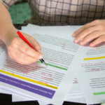 A close-up of a person using a red pen to proofread an academic paper, demonstrating essential assignment tips for students.
