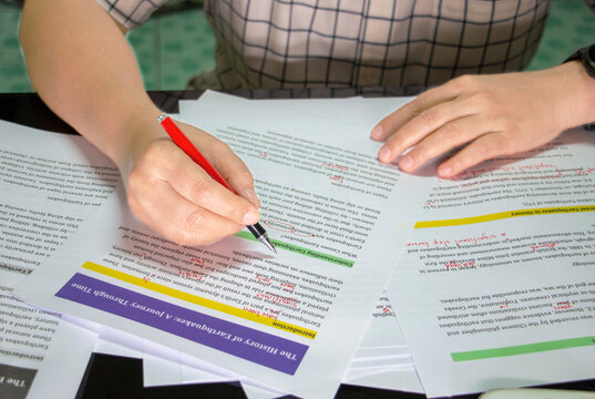 A close-up of a person using a red pen to proofread an academic paper, demonstrating essential assignment tips for students.