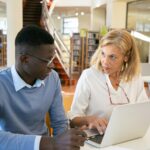 A student receiving one-on-one academic guidance from a professional tutor in a library setting.