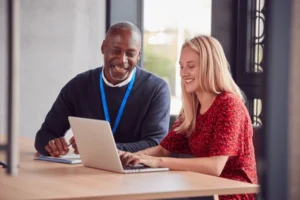 A female college student receiving professional assignment help from a male academic tutor while working on a laptop.