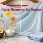 Georgette saree with turmeric, oil, and tea stains beside lemon, vinegar, and cornstarch remedies on marble surface, showing before-and-after stain removal.