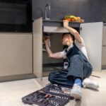 Man reclining inspecting pipe under kitchen sink