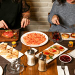 two women have breakfast with toasts crepes pancakes jam and scrambled eggs