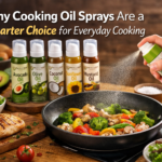 Cooking oil spray being used on a pan of sautéed vegetables, with bottles of avocado, olive, coconut, sunflower, and mustard oil sprays displayed alongside grilled chicken and fresh ingredients.