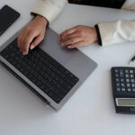 Person working on a modern laptop, typing and calculating data on a desk