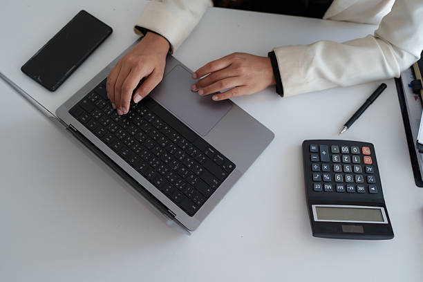Person working on a modern laptop, typing and calculating data on a desk