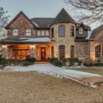 Luxury two-story brick home with turret-style architecture, landscaped front yard, and curved walkway leading to a warmly lit entrance at dusk