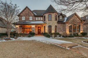 Luxury two-story brick home with turret-style architecture, landscaped front yard, and curved walkway leading to a warmly lit entrance at dusk