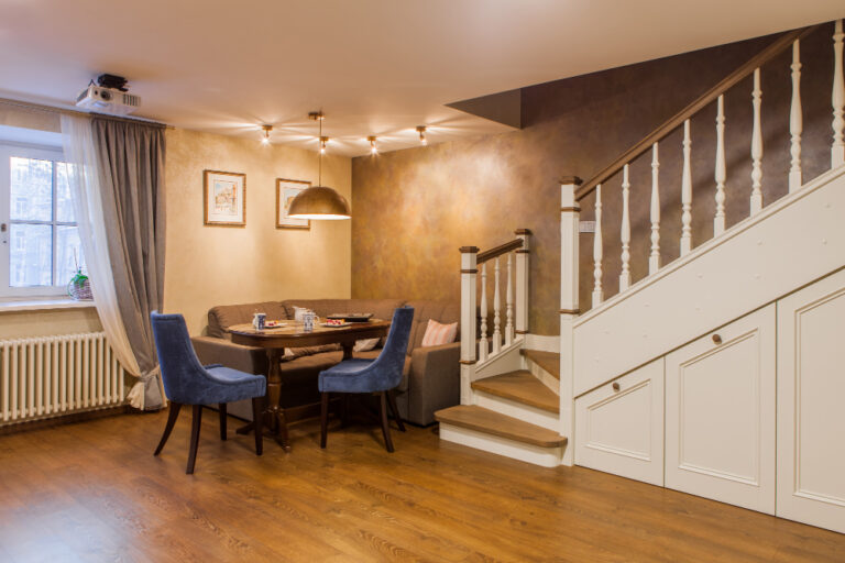 Cozy finished basement with wooden flooring, dining area, upholstered seating, and staircase with white railing and built-in storage underneath