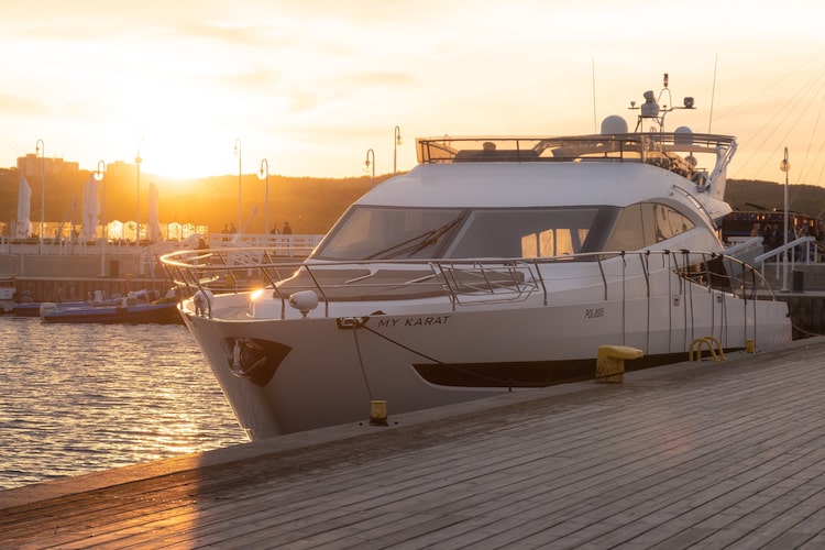Luxury yacht docked at a marina during sunset, with golden sunlight reflecting on the water and pier in the foreground.