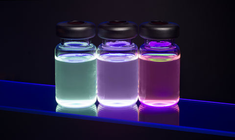 hree glowing vials containing fluorescent quantum dot nanocrystal solutions emitting blue, purple, and pink light.
