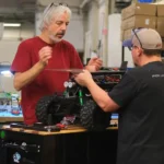 Two engineers collaborating on the assembly and testing of a large remote-controlled robotic vehicle in a workshop environment.