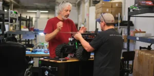 Two engineers collaborating on the assembly and testing of a large remote-controlled robotic vehicle in a workshop environment.