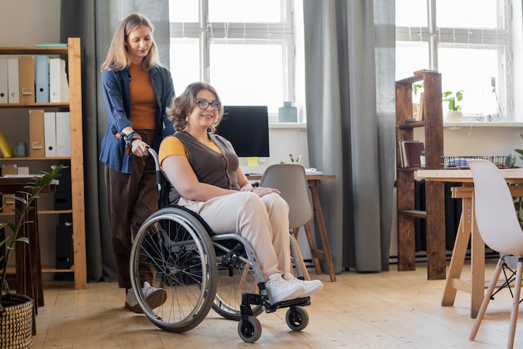 young-smiling-woman-wheelchair-looking-forwards-while-her-sister-friend-standing-helping-her-with-moving-around_274679-17610