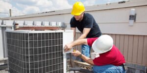 HVAC technicians inspecting and repairing an outdoor air conditioning unit on a rooftop.