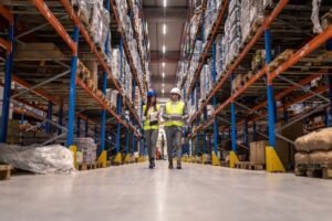workers-with-hardhats-reflective-jackets-walking-through-big-warehouse-aisle-checking-goods-condition