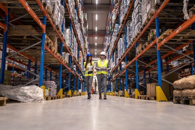 workers-with-hardhats-reflective-jackets-walking-through-big-warehouse-aisle-checking-goods-condition