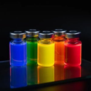 Colorful laboratory vials containing blue, green, yellow, orange, and red quantum dot solutions on a reflective surface.
